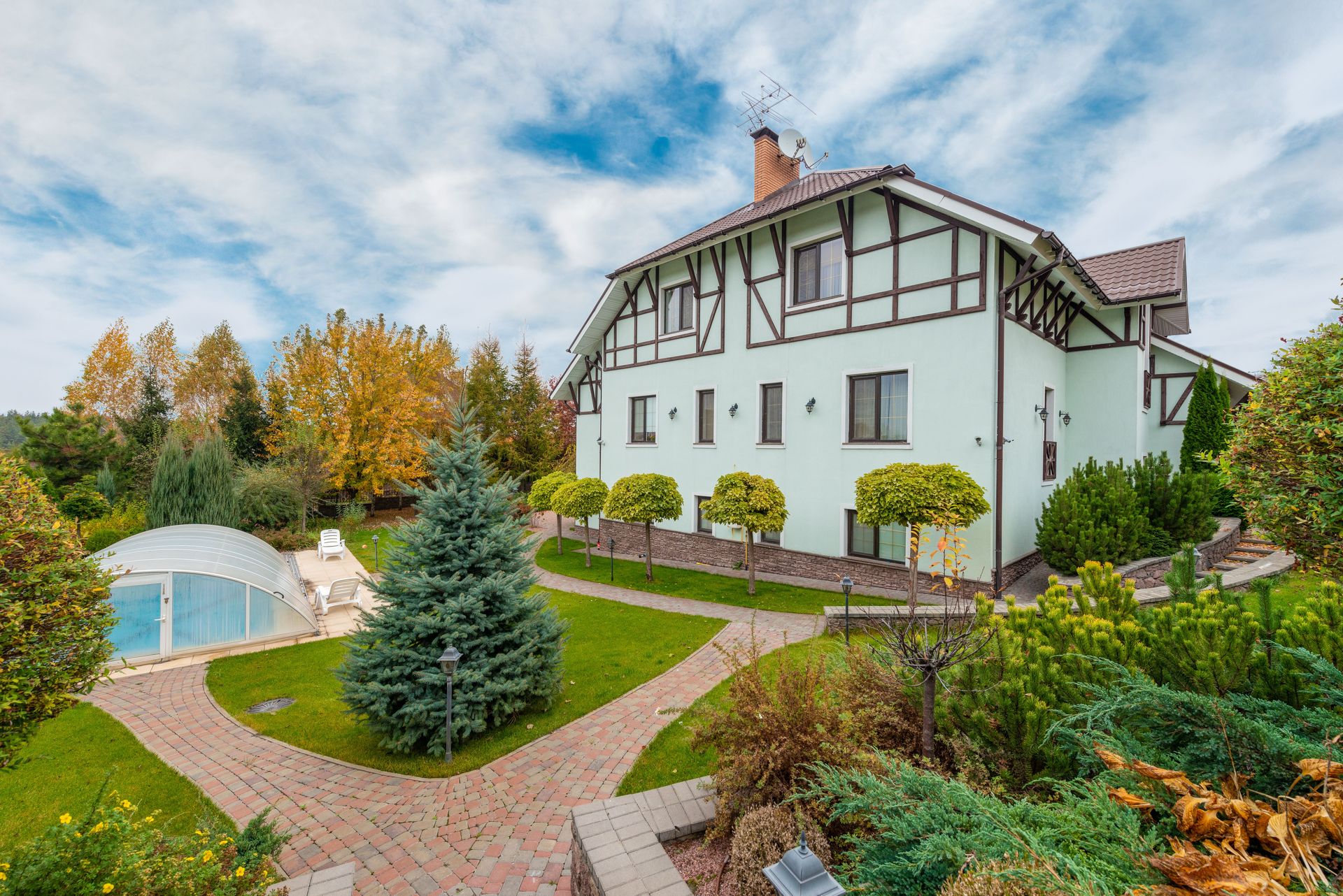Tudor-style home with landscaped garden and pool under a vibrant cloudy sky.